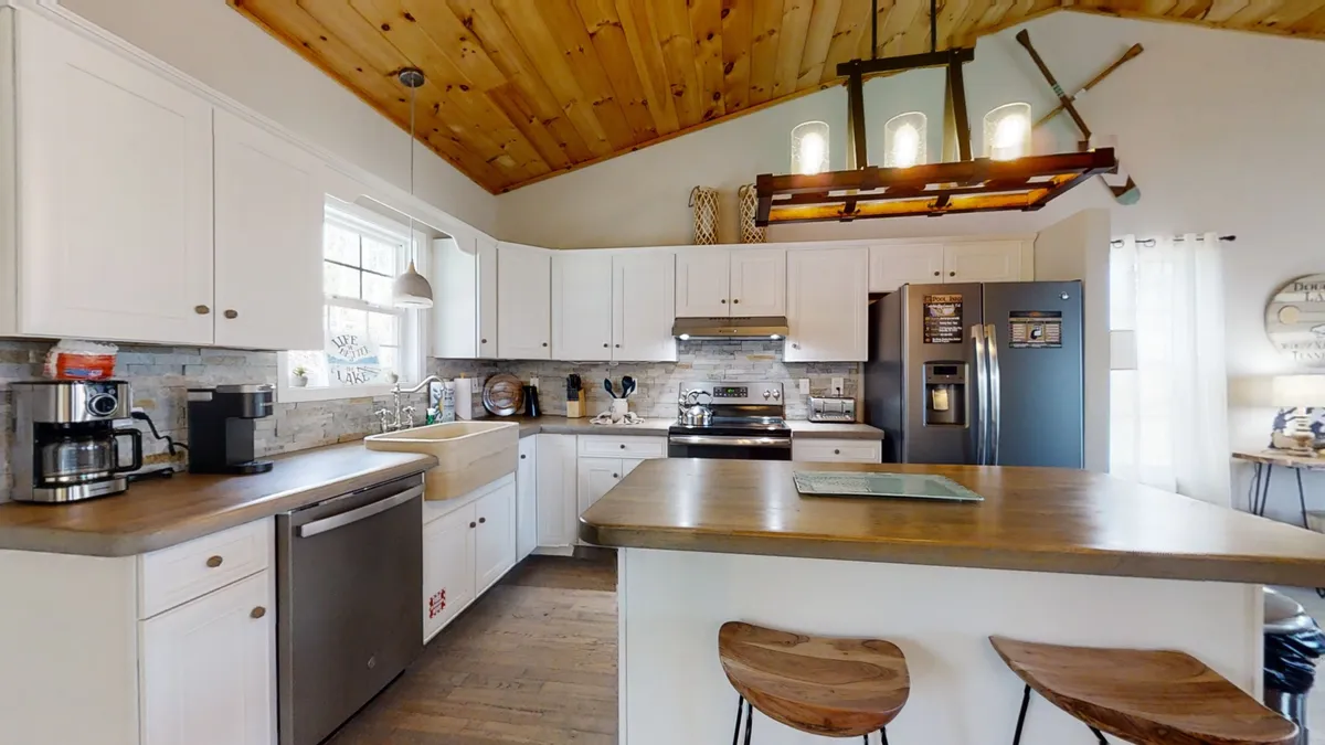 A warmly lit kitchen featuring a central island, hanging light fixture, modern appliances, coffee maker, and plenty of cabinetry. The inviting space is ideal for both cooking and casual gatherings, with a layout that encourages interaction and shared activities.