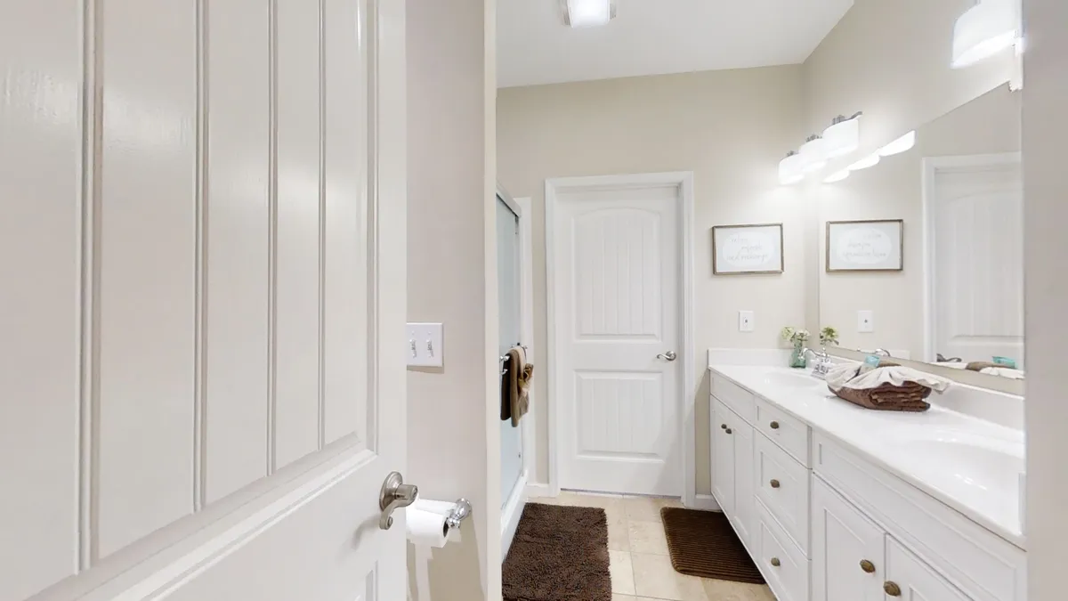 A bright, modern bathroom featuring a vanity with double sinks, a spacious shower area, framed wall art, and neatly organized amenities. The clean lines and soothing colors create a spa-like feel, emphasizing both function and relaxation.