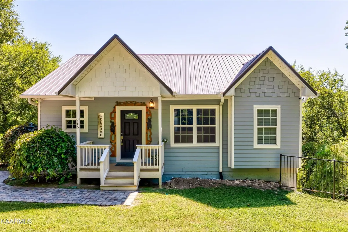 An inviting front porch welcomes you with its rustic decor, a prominent welcome sign, and carefully maintained landscaping. The setting suggests a relaxing transition from indoors to outdoors, suitable for sipping coffee or enjoying quiet moments surrounded by nature.