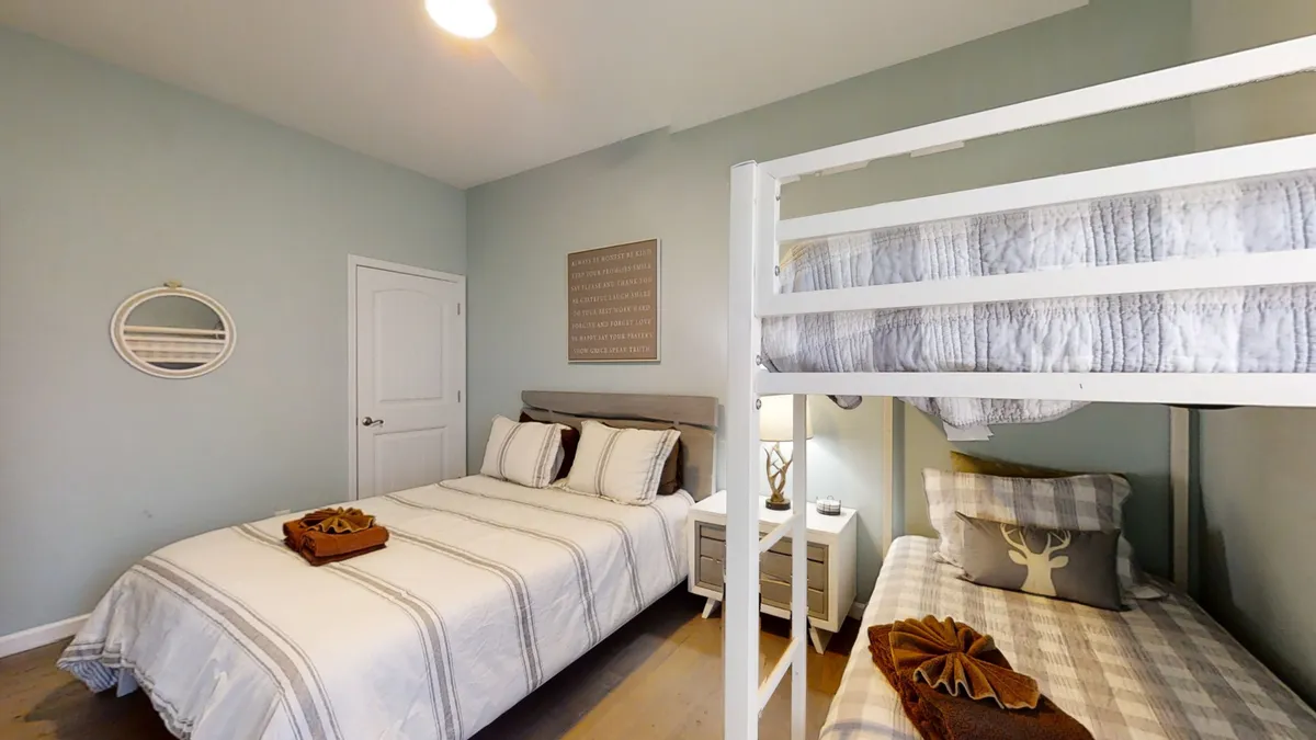 A family-friendly bedroom featuring a bunk bed and a double bed, accented by playful decorative wall art and a nightstand. The space feels cozy and inviting, perfect for family bonding and restful nights after days spent exploring nearby lakes and trails.