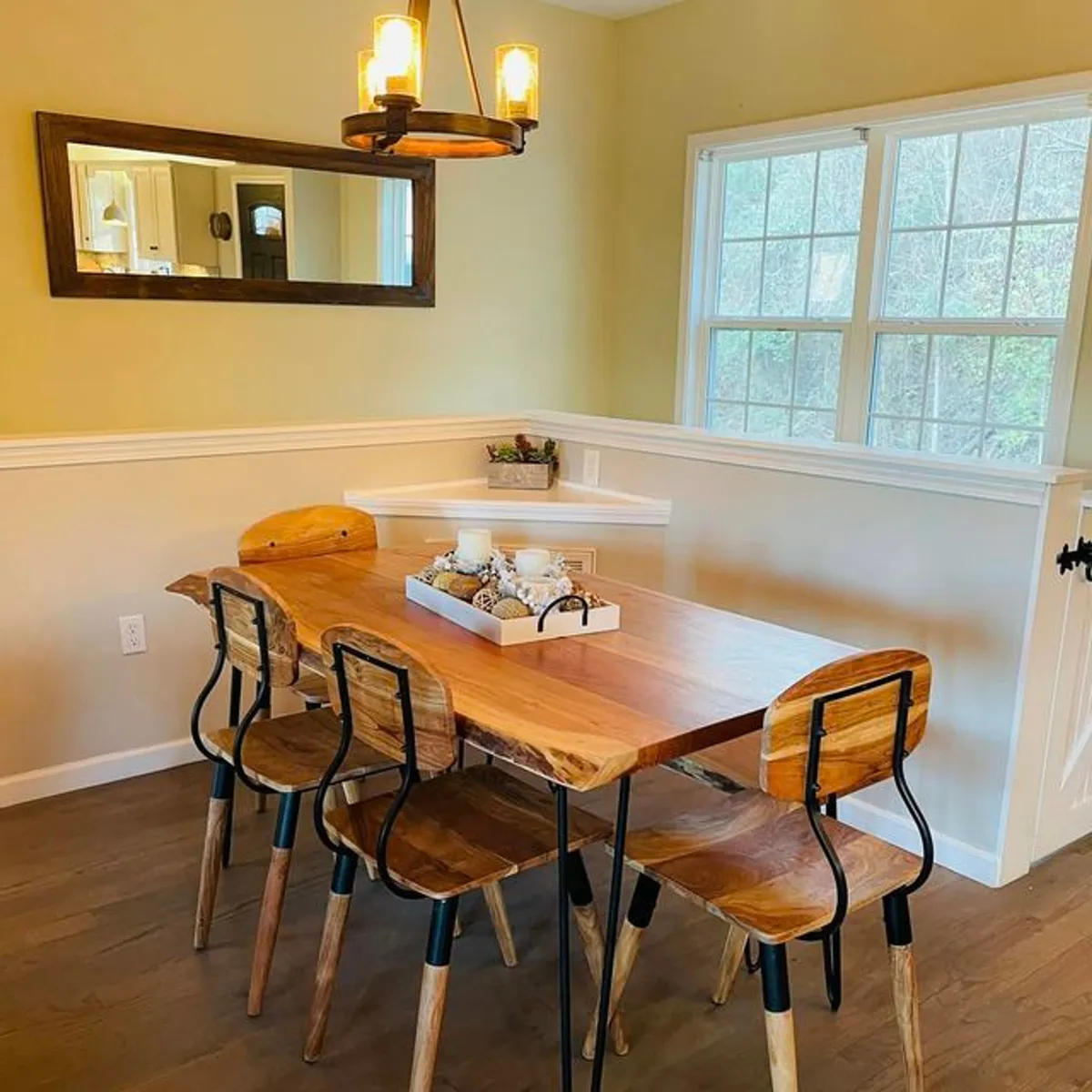A cozy dining area with a wooden table set beneath a chandelier, mirrored wall, and a decorative tray centerpiece. The space is intimate yet open, inviting family meals, holiday celebrations, and relaxed coffee chats.