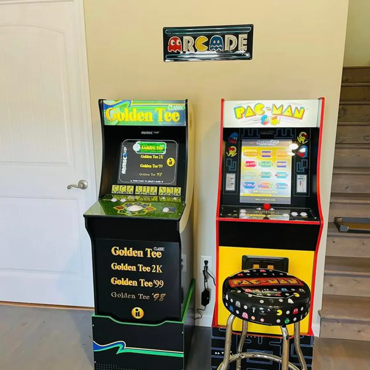 A vibrant game room featuring both the Golden Tee and Pac-Man arcade machines, a colorful arcade-inspired sign, and a playful bar stool. The setup invites lively activity and friendly competition, with retro touches that evoke nostalgia and fun.